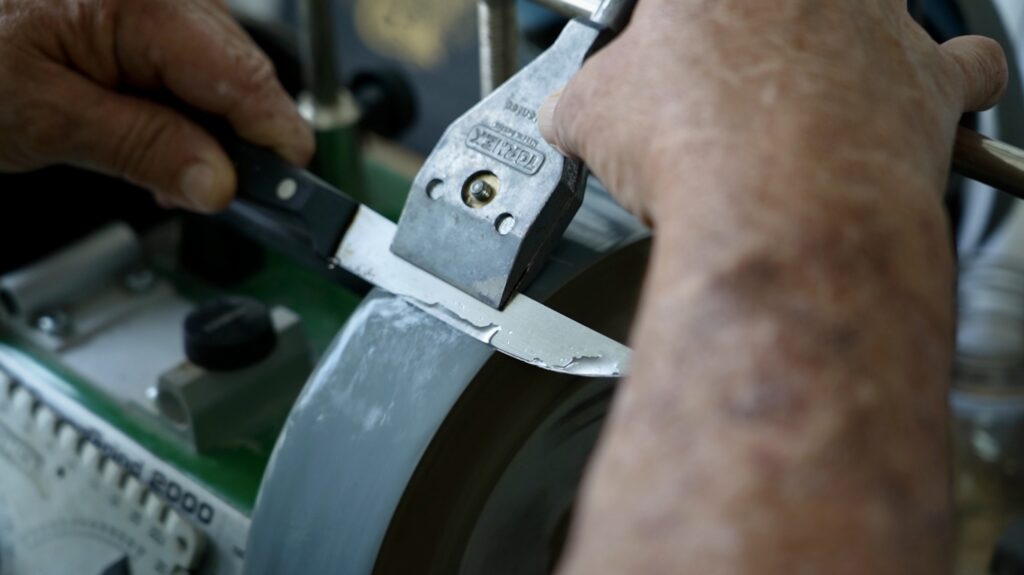 A pair of hands sharpening a knife using the water honing machine.