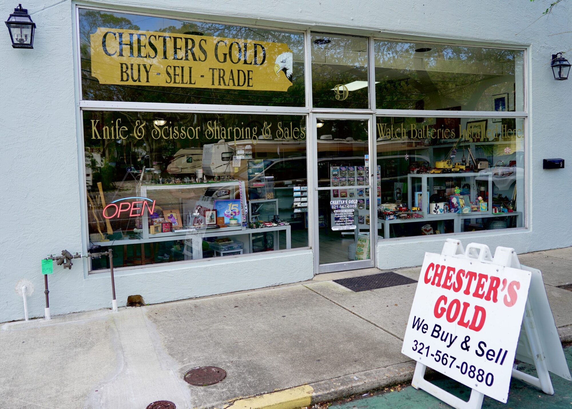 A storefront of Chester's Gold with Knife & Scissor Sharping & Sales Watch Batteries and a sign out front that says Chester's Gold We Buy & Sell 321-567-0880.